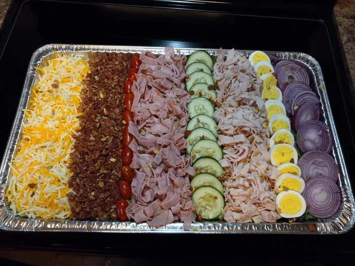 A tray of rolled deli meats, cheeses, cucumber and egg slices