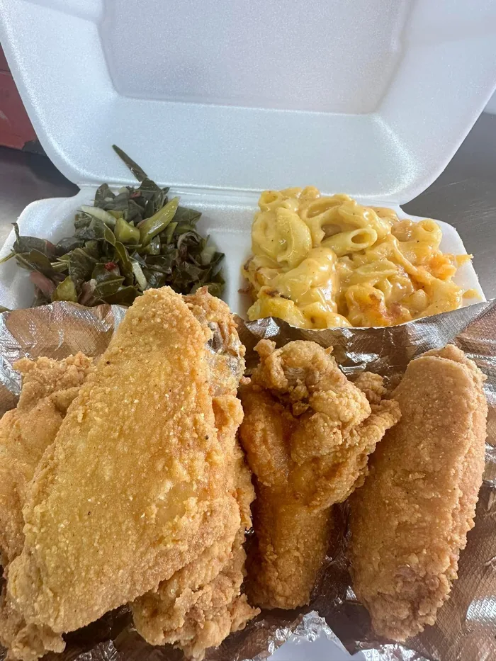 A takeout box of Southern fried chicken with collard greens and macaroni and cheese